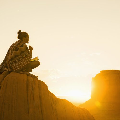 佩带被仿造的披肩的妇女，当坐在小山的一个期刊时，当太阳上升时
