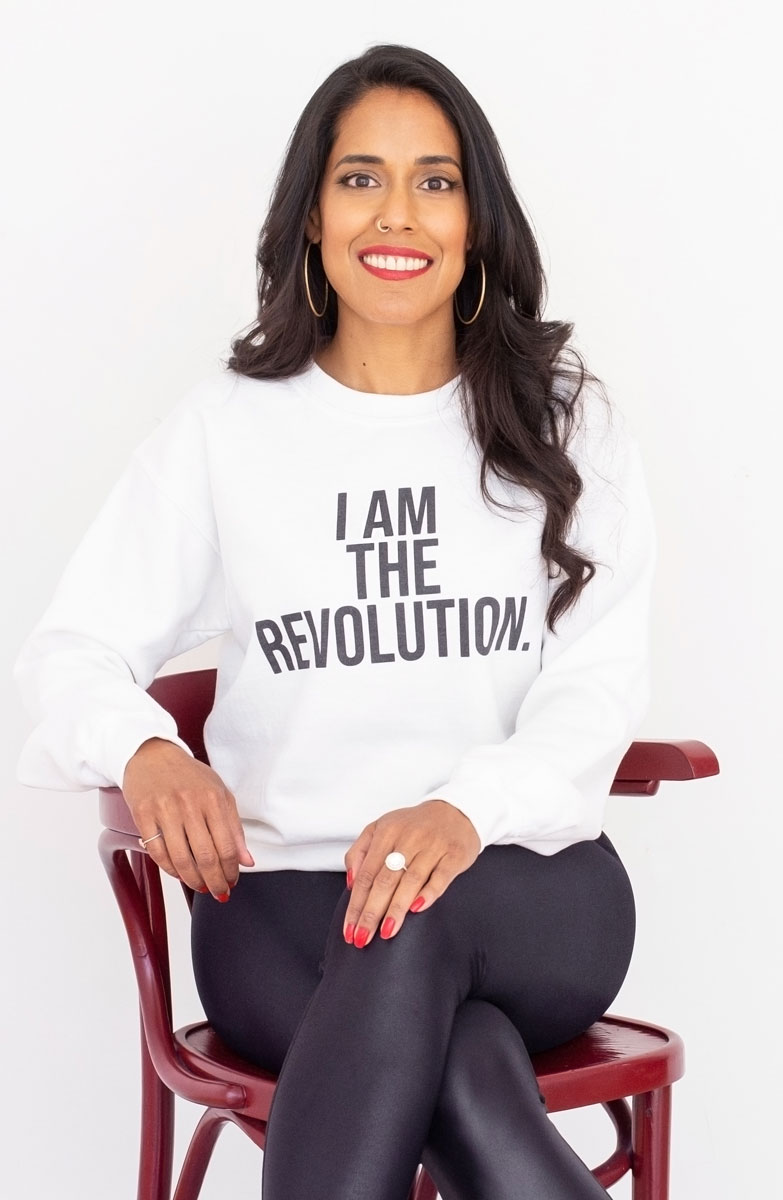 beplay体育手机里图·哈辛舒适地坐在椅子上，穿着一件写着“我是革命”的白色运动衫，对着镜头微笑。