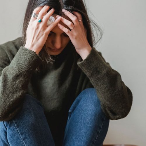 A young woman looking upset as she holds her head in her hands and looks down.