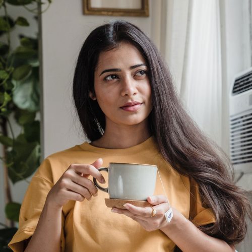 A young brown woman wearing a yellow shirt holding a white mug with both hands