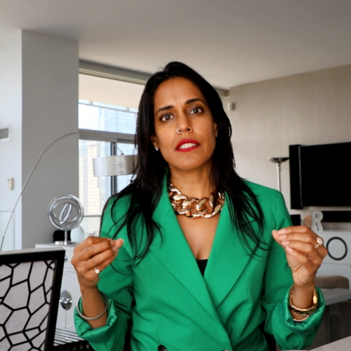 Ritu Bhasin wearing a bright green blazer and gold necklace, looking into the camera with both hands raised.
